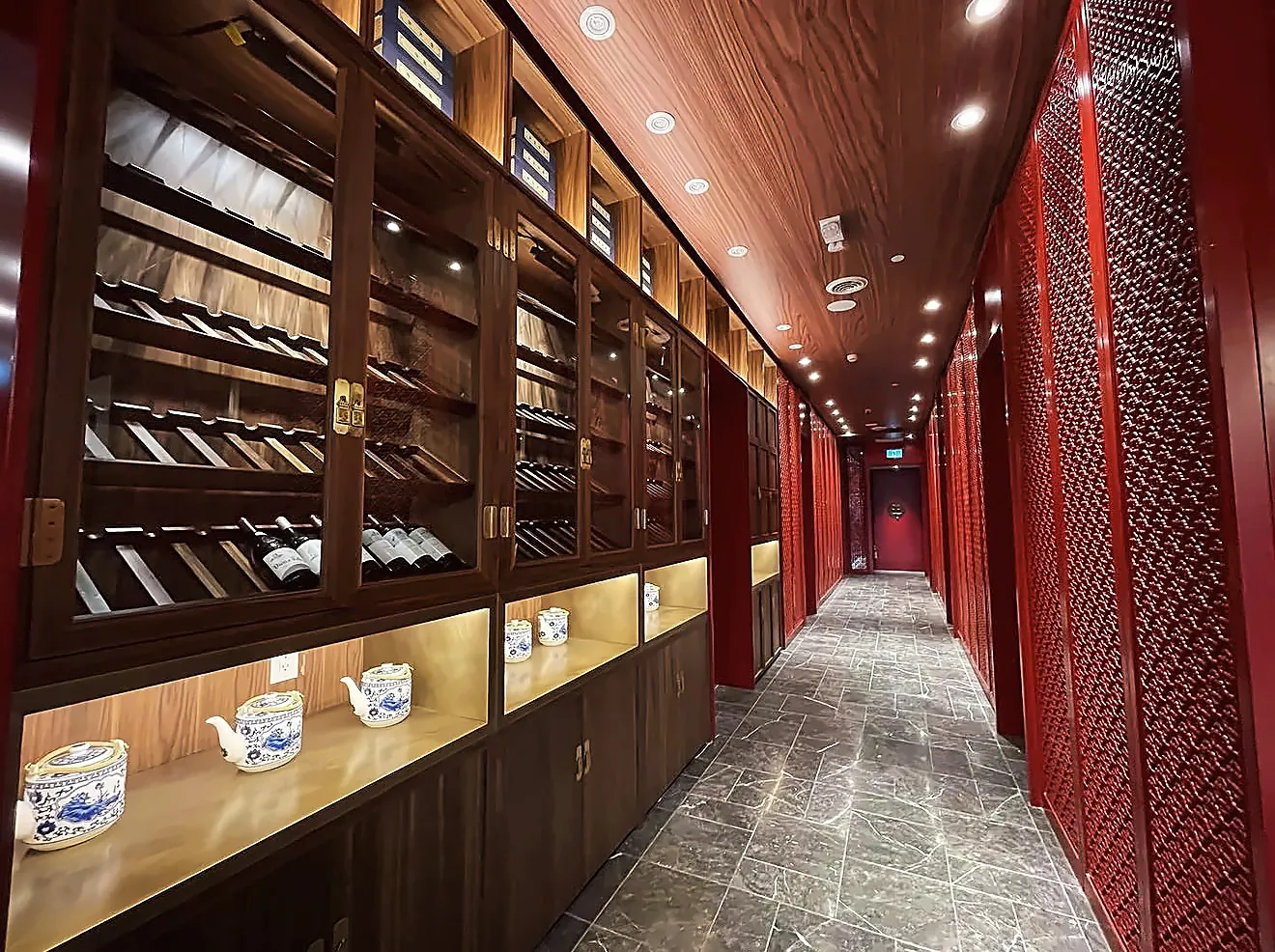 Le couloir menant aux salons privés : vitrines à vin d’un côté, panneaux rouges ajourés de l’autre